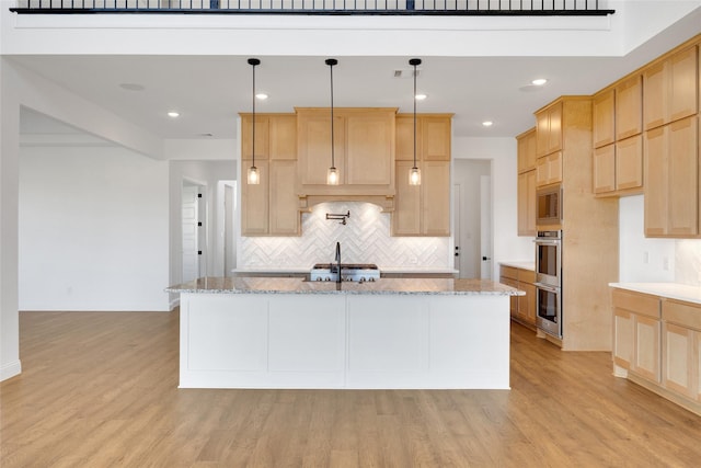 kitchen with light stone counters, a center island with sink, hanging light fixtures, and light hardwood / wood-style flooring