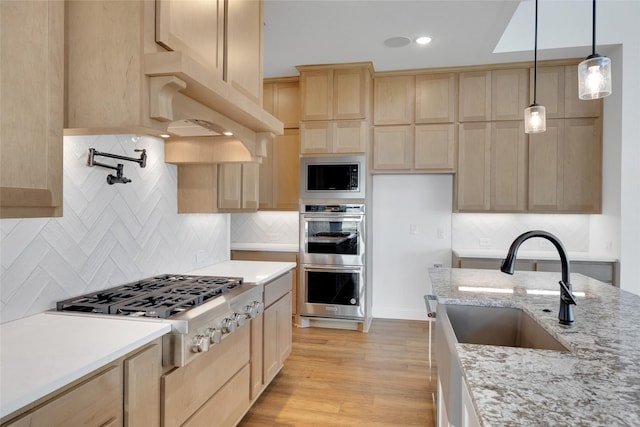 kitchen with pendant lighting, light brown cabinets, sink, light stone countertops, and stainless steel appliances