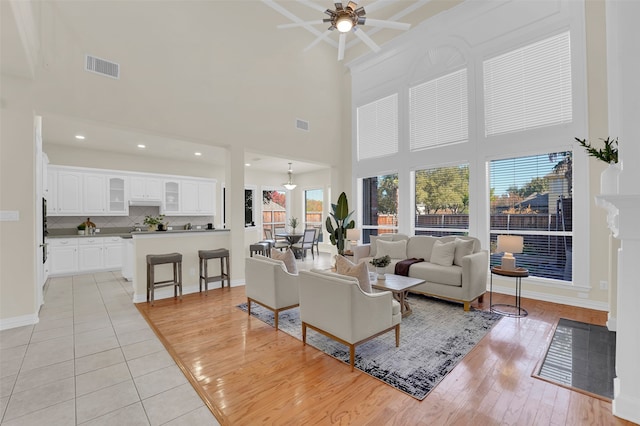 living room with ceiling fan, light hardwood / wood-style floors, and a high ceiling