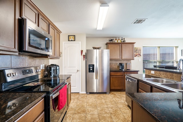 kitchen featuring decorative backsplash, stainless steel appliances, dark stone counters, and sink