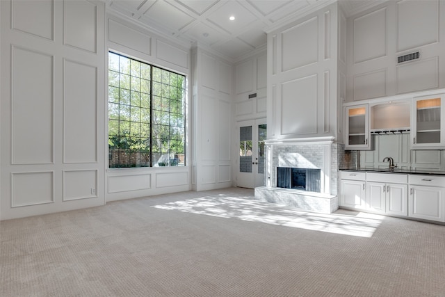 unfurnished living room featuring a fireplace, light colored carpet, coffered ceiling, and sink