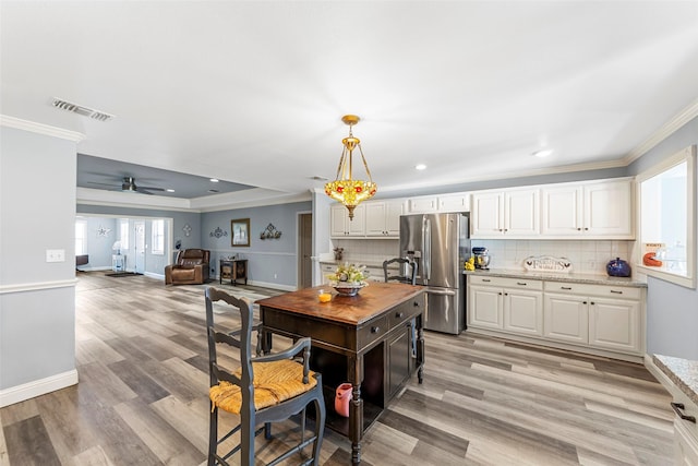 kitchen with white cabinets, decorative light fixtures, stainless steel refrigerator, and tasteful backsplash