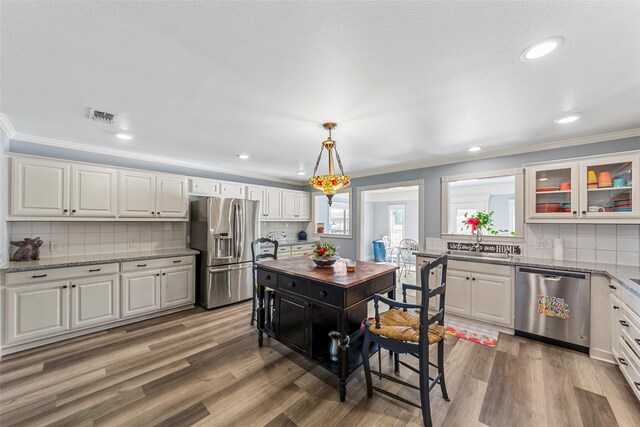 kitchen featuring appliances with stainless steel finishes, tasteful backsplash, hardwood / wood-style floors, white cabinetry, and hanging light fixtures