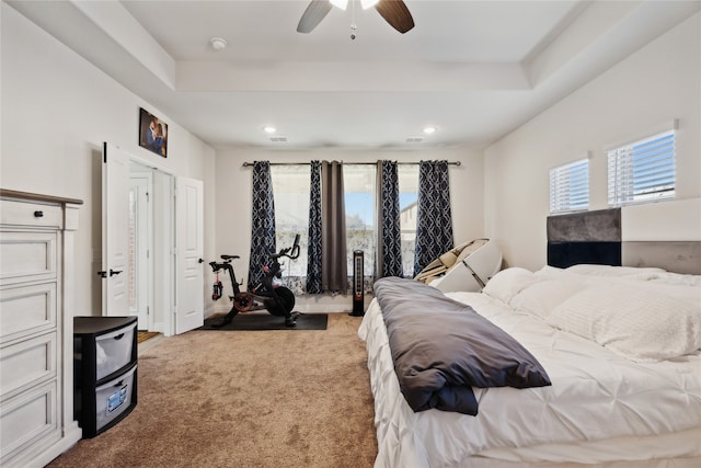 bedroom with light colored carpet, a raised ceiling, and ceiling fan