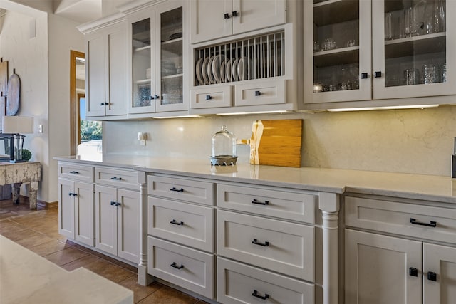 interior space with tile patterned floors, light stone countertops, white cabinetry, and backsplash