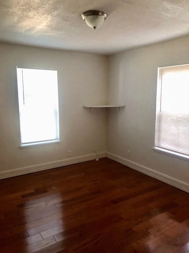 empty room with a textured ceiling, plenty of natural light, and dark wood-type flooring