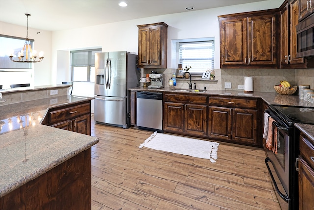 kitchen featuring dark stone counters, an inviting chandelier, sink, light wood-type flooring, and appliances with stainless steel finishes