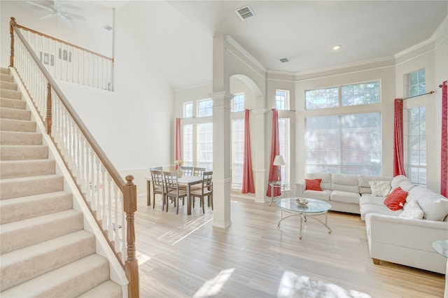 living room with hardwood / wood-style floors, ceiling fan, a towering ceiling, ornamental molding, and decorative columns