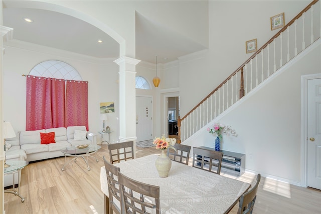 dining room with ornate columns, crown molding, a towering ceiling, and hardwood / wood-style flooring