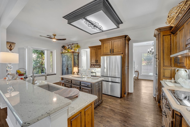 kitchen featuring light stone countertops, stainless steel fridge, dark hardwood / wood-style flooring, ceiling fan with notable chandelier, and a kitchen island