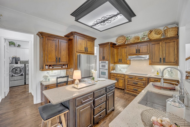 kitchen with a kitchen island, sink, washing machine and dryer, dark hardwood / wood-style floors, and stainless steel refrigerator