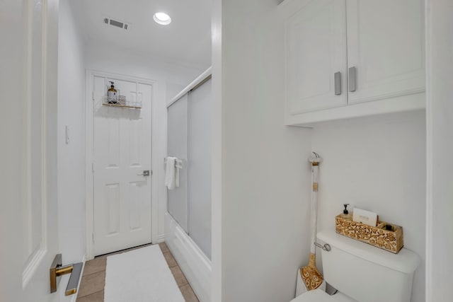 bathroom with tile patterned floors, shower / bath combination with glass door, and toilet