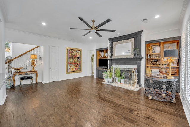 living room featuring dark hardwood / wood-style floors, a large fireplace, crown molding, and ceiling fan