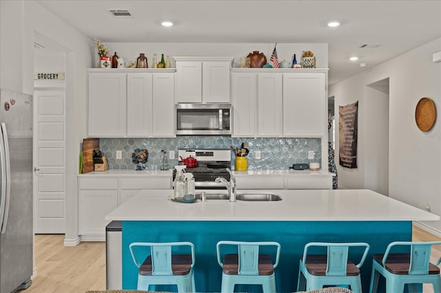 kitchen featuring a center island with sink, white cabinets, decorative backsplash, appliances with stainless steel finishes, and light hardwood / wood-style floors