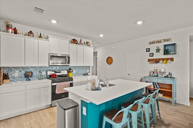 kitchen featuring backsplash, white cabinets, light hardwood / wood-style flooring, an island with sink, and appliances with stainless steel finishes