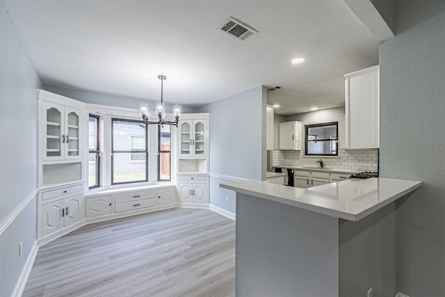 kitchen featuring white cabinetry, light hardwood / wood-style flooring, backsplash, kitchen peninsula, and pendant lighting