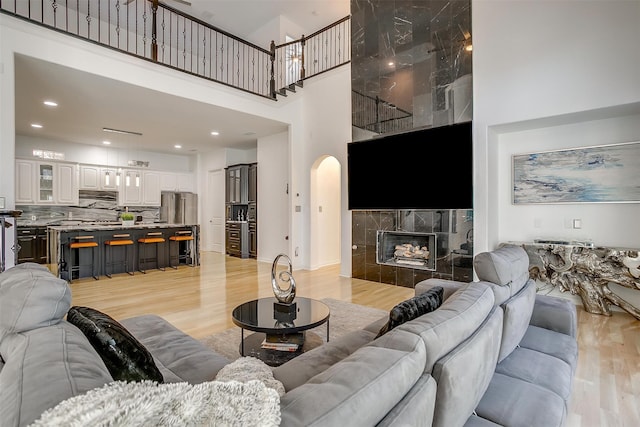 living room featuring a tile fireplace, light hardwood / wood-style floors, and a high ceiling