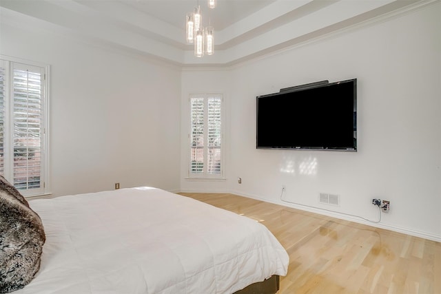 bedroom featuring a chandelier, hardwood / wood-style flooring, a tray ceiling, and crown molding