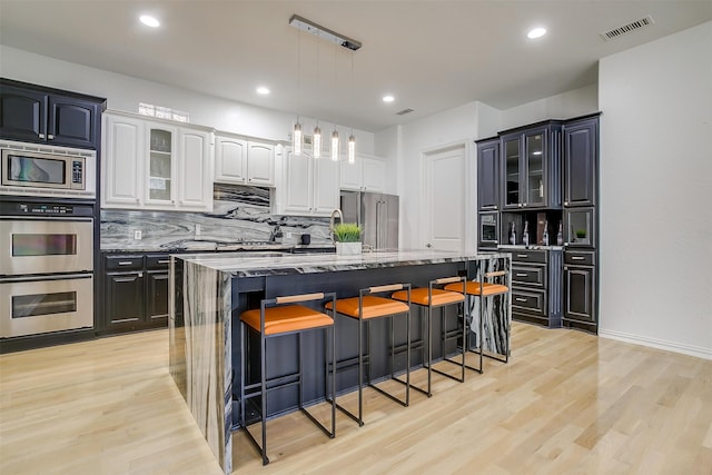 kitchen featuring backsplash, a kitchen island with sink, white cabinets, appliances with stainless steel finishes, and light hardwood / wood-style floors