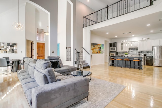 living room with light hardwood / wood-style flooring, a towering ceiling, and a chandelier