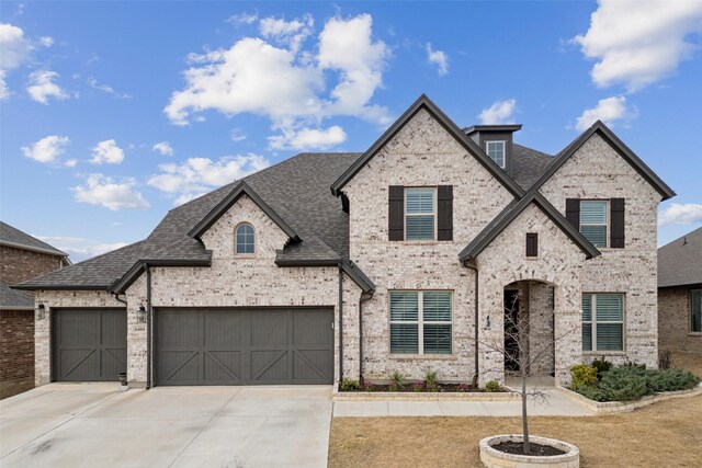 french country style house with a front yard, concrete driveway, brick siding, and fence