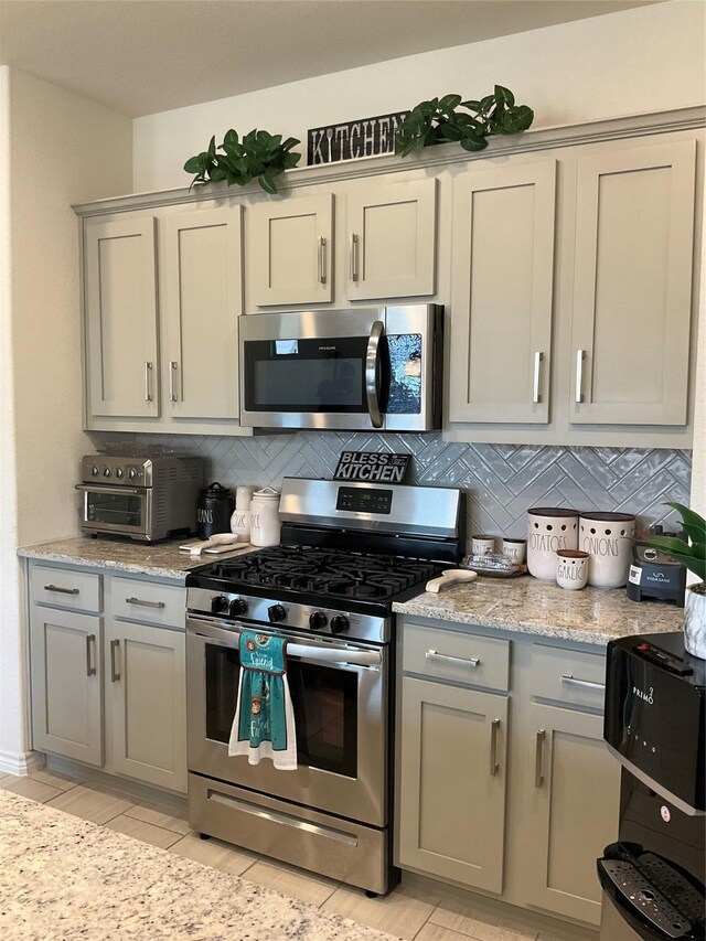 kitchen with light stone countertops, backsplash, stainless steel appliances, and gray cabinetry