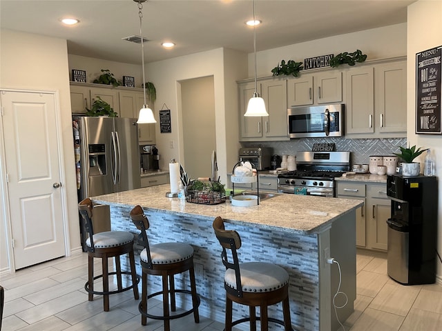 kitchen featuring decorative light fixtures, gray cabinets, stainless steel appliances, and an island with sink