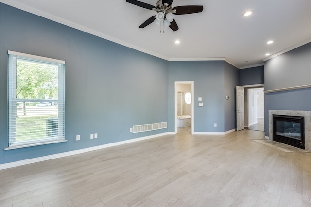 unfurnished living room featuring a tiled fireplace, crown molding, and light wood-type flooring