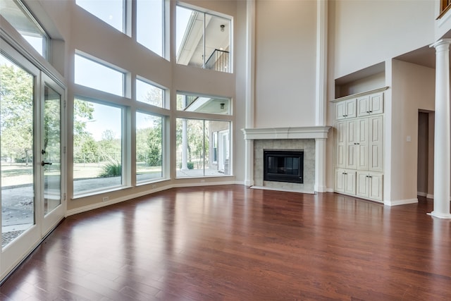 unfurnished living room with decorative columns, a tile fireplace, a high ceiling, and dark hardwood / wood-style floors