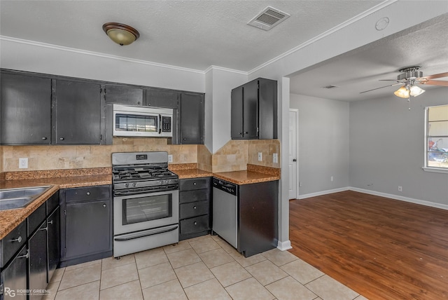 kitchen featuring ceiling fan, light tile patterned floors, a textured ceiling, appliances with stainless steel finishes, and decorative backsplash