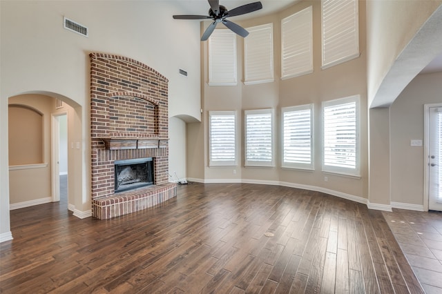 unfurnished living room featuring ceiling fan, dark hardwood / wood-style flooring, a high ceiling, and a brick fireplace