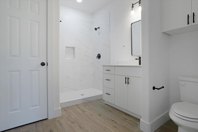 bathroom featuring tiled shower, toilet, vanity, and hardwood / wood-style flooring