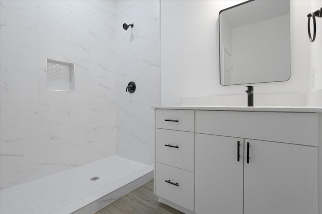 bathroom with wood-type flooring, vanity, and a tile shower