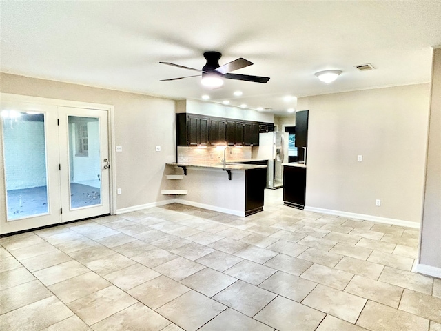 kitchen featuring a breakfast bar, backsplash, ceiling fan, stainless steel fridge, and kitchen peninsula