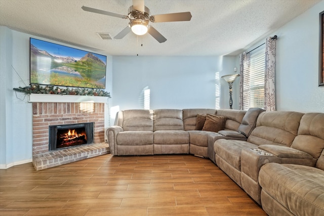 living room with ceiling fan, a brick fireplace, a textured ceiling, and light hardwood / wood-style floors