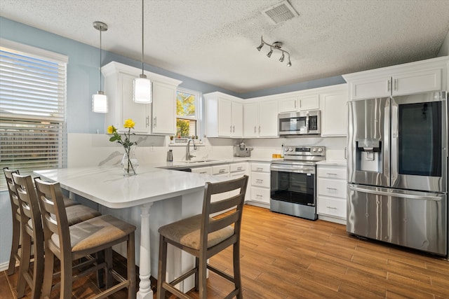 kitchen with pendant lighting, appliances with stainless steel finishes, white cabinetry, wood-type flooring, and kitchen peninsula