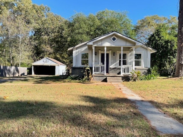 bungalow-style home featuring a porch, a garage, an outdoor structure, and a front lawn