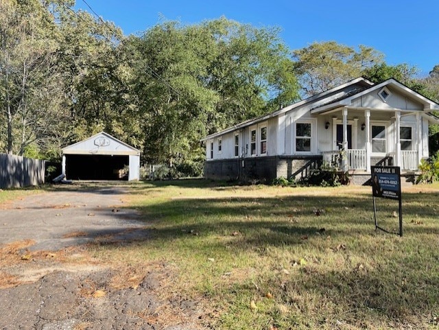 view of front of house featuring covered porch, a garage, a front lawn, and an outdoor structure