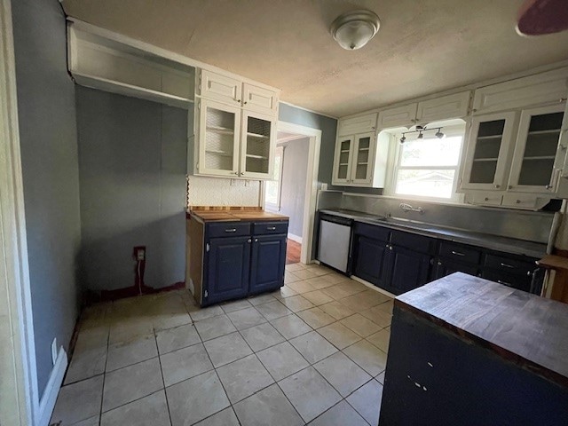 kitchen with butcher block countertops, white cabinets, stainless steel dishwasher, and light tile patterned floors