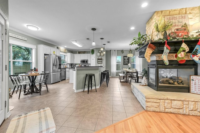 interior space featuring white cabinetry, appliances with stainless steel finishes, pendant lighting, light tile patterned floors, and ornamental molding