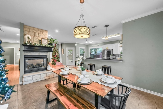 tiled dining space featuring a stone fireplace and ornamental molding