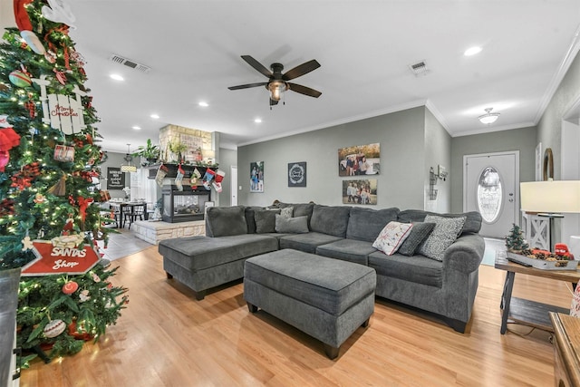 living room featuring a fireplace, ceiling fan, crown molding, and light hardwood / wood-style floors