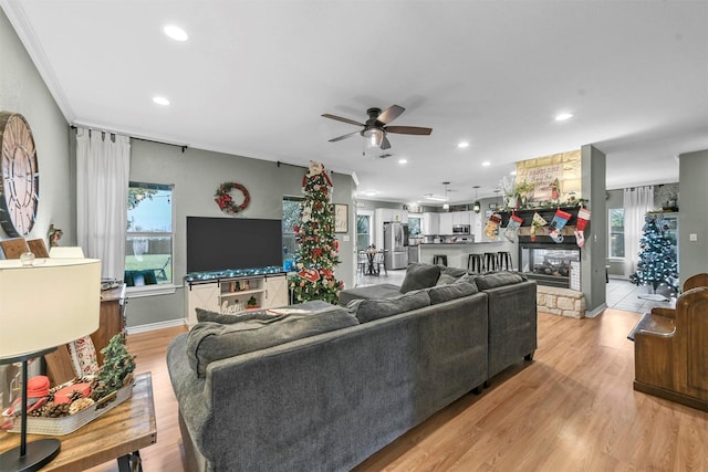 living room featuring a stone fireplace, ceiling fan, crown molding, and light wood-type flooring