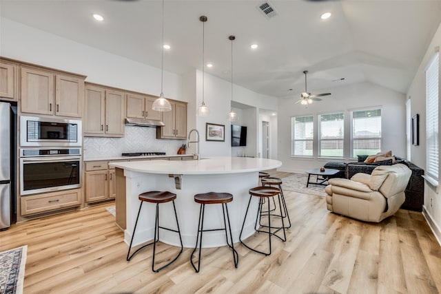 kitchen featuring light brown cabinetry, an island with sink, lofted ceiling, and appliances with stainless steel finishes