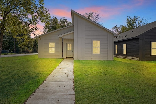 back house at dusk featuring a lawn