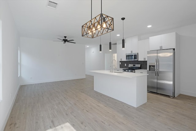 kitchen featuring stainless steel appliances, ceiling fan, sink, decorative light fixtures, and an island with sink