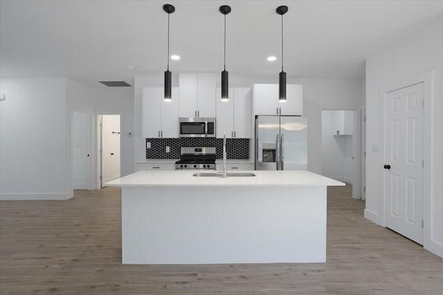 kitchen featuring appliances with stainless steel finishes, decorative light fixtures, light hardwood / wood-style floors, and an island with sink