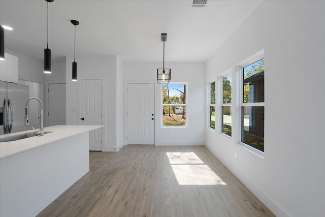 kitchen featuring stainless steel fridge, light hardwood / wood-style flooring, hanging light fixtures, and sink