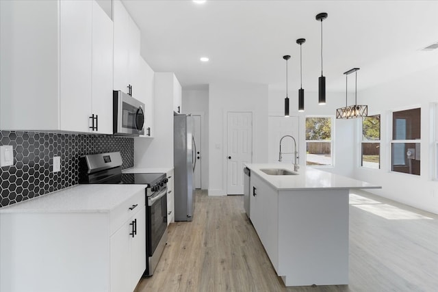 kitchen featuring sink, light hardwood / wood-style flooring, an island with sink, decorative light fixtures, and stainless steel appliances