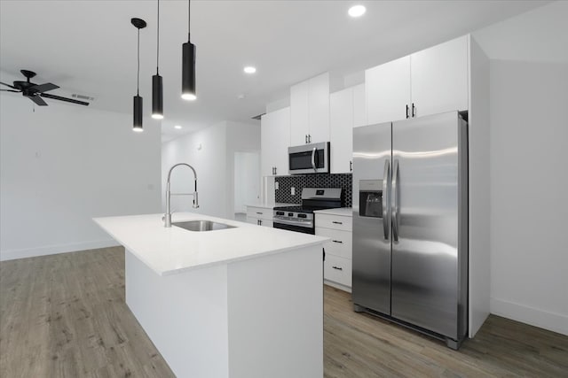 kitchen featuring stainless steel appliances, sink, light hardwood / wood-style floors, hanging light fixtures, and an island with sink